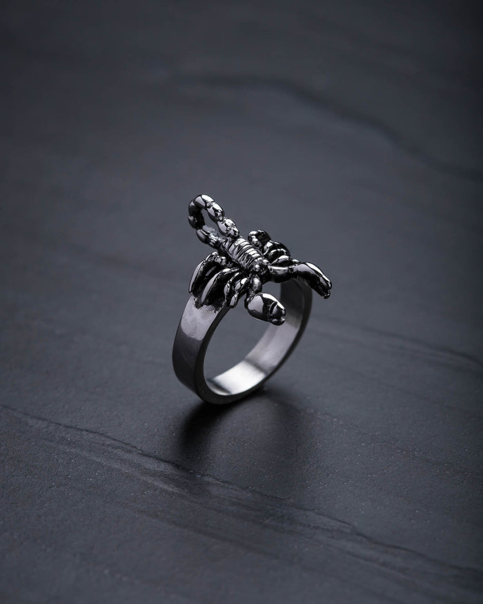 The Scorpion Ring features a detailed design and stands upright on a dark, textured surface—an eye-catching piece for scorpion jewelry lovers.