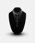 Statement Collective’s Sharp Objects Set is shown on a black velvet necklace display stand, featuring five layered silver chains including a bold Cuban link chain and assorted pendant necklaces with swords, crosses, and geometric accents, all set against a clean white background.