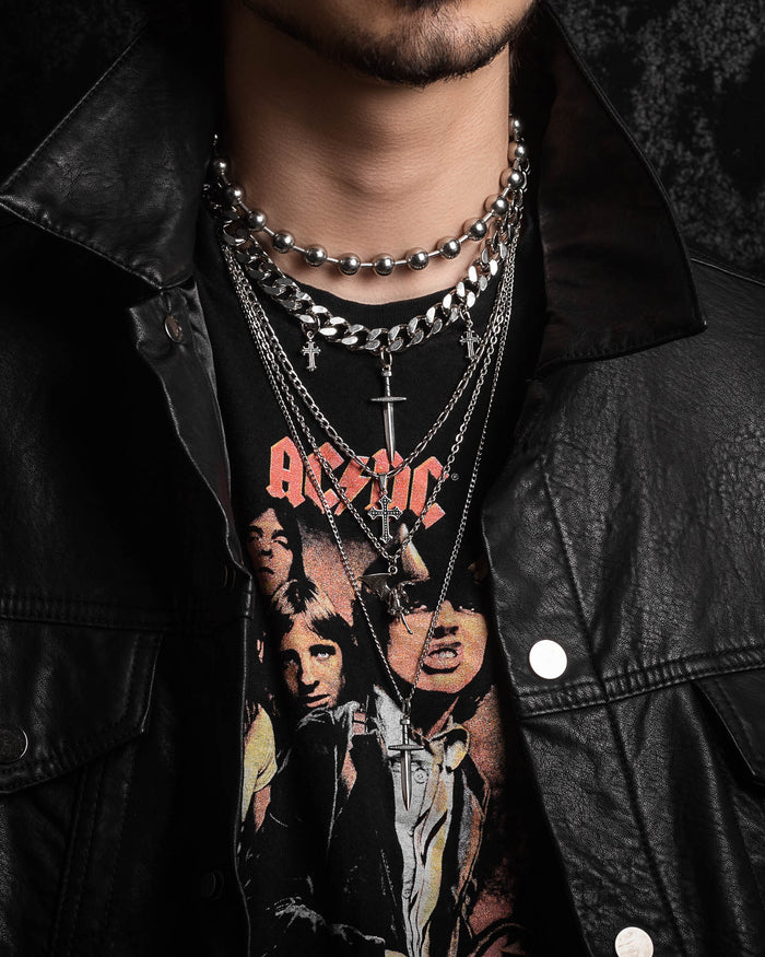 A person wearing the Statement Collective Sharp Objects Set—layered silver necklaces featuring a striking Cuban link chain—paired with a black leather jacket and a black AC/DC band t-shirt with images of the band members.