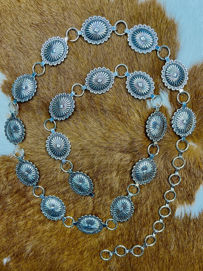 Small to medium silver concho belt coiled on cowhide showing the full chain length