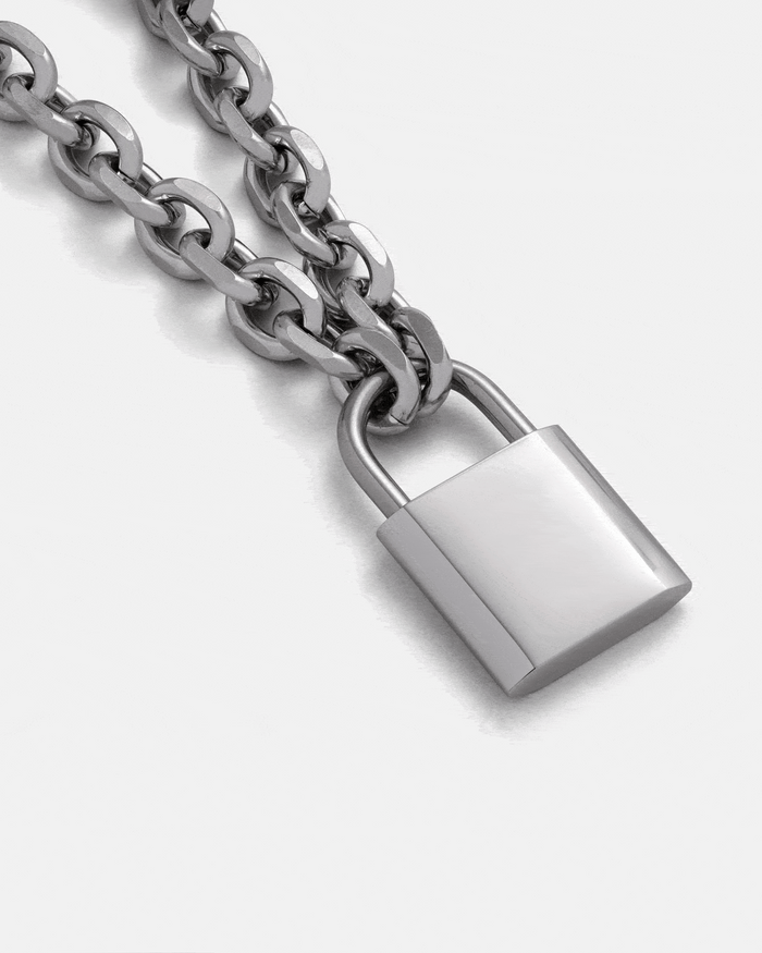 A close-up of the Statement Collective Statement Lock & Chain 2.0 silver necklace, showcasing its shiny padlock pendant—perfect statement jewelry displayed against a plain light background.