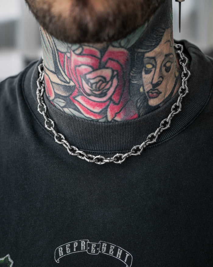 Close-up of a person’s neck with colorful tattoos, wearing "The Cathedral" 9mm Spiked Chain and a black shirt with “REPRESENT” printed on it.