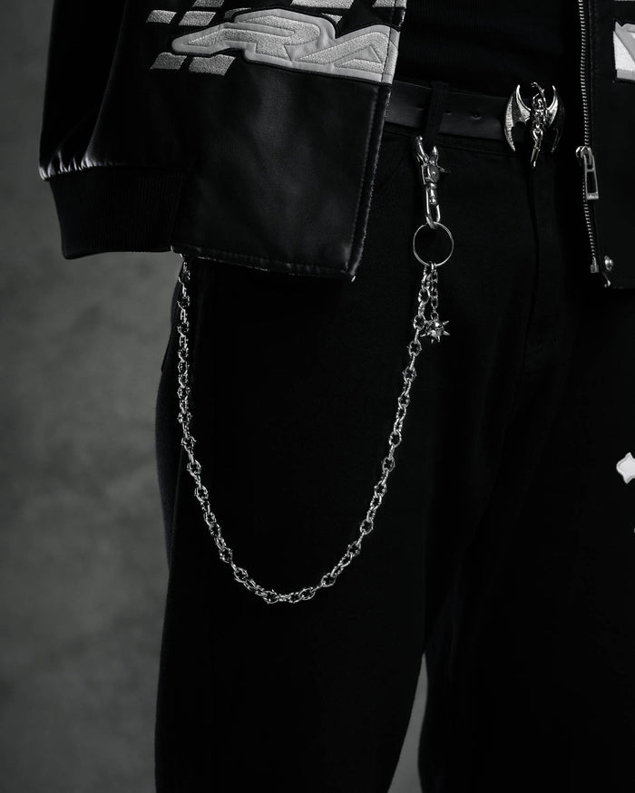 A close-up of a person wearing black pants and a black leather jacket with metallic details, featuring "The Cathedral" 9mm Spiked Wallet Chain hooked to the belt loop, set against a dark background.