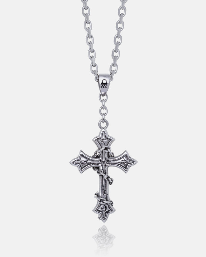 The Ruins" Pendant features an ornate, gothic cross with intricate detailing on a silver chain, shown against a white background. This large necklace is a bold statement piece for any collection.
